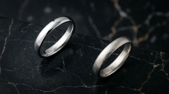 Deux alliances en or blanc posées côte à côte sur une surface de marbre, avec des effets de lumière différents