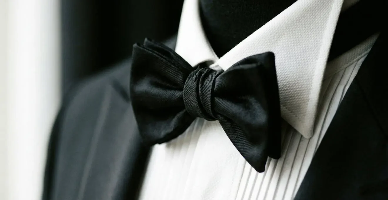 Gros plan sur un col cassé de chemise blanche avec nœud papillon noir et plastron plissé