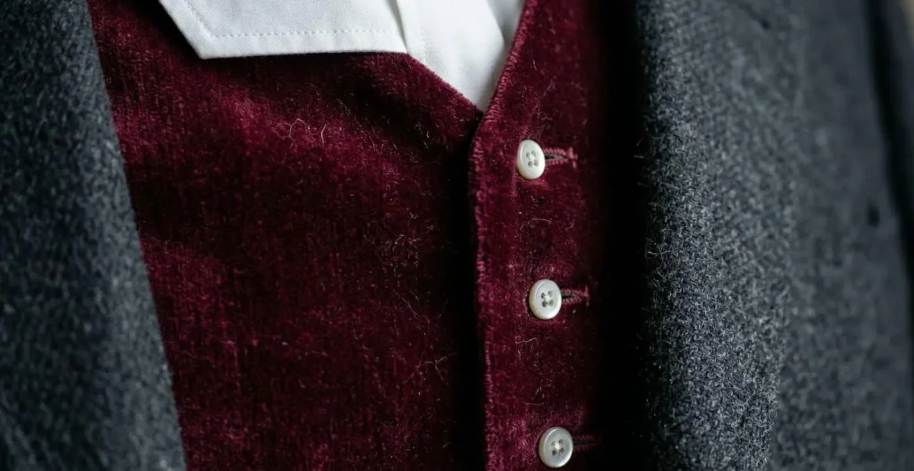 Détail rapproché d'un gilet en velours bordeaux contrastant avec une redingote en laine gris anthracite
